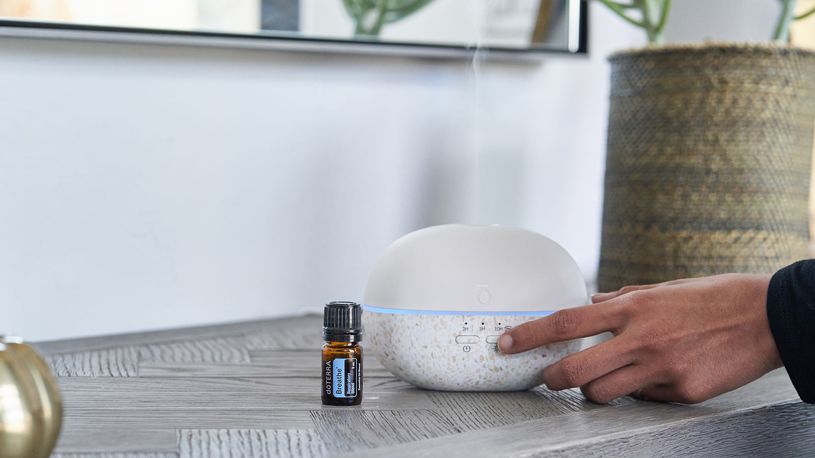 A woman pressing her finger against the doTERRA Pebble Diffuser as mist comes out from the top. Breathe essential oil blend sits to the side of the diffuser. 