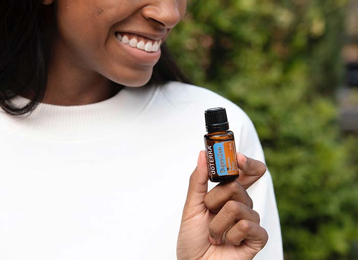 A woman holding doTERRA DigestZen and lifting the side of her shirt with one hand, while rubbing the essential oil on with the other hand. 