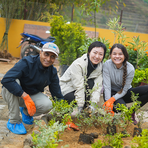 One man and two women squatted down on a cement path in a garden, pause their planting to pose for the photo. 
