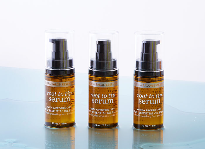 Three bottles of Root to Tip Serum sitting on a wet, light blue surface. 