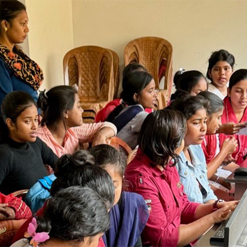 A group of women attentively watching a laptop presentation, led by another woman in a classroom setting.