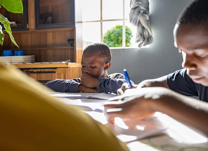 Two boys kneeling on the ground, up against a table, doing homework. 