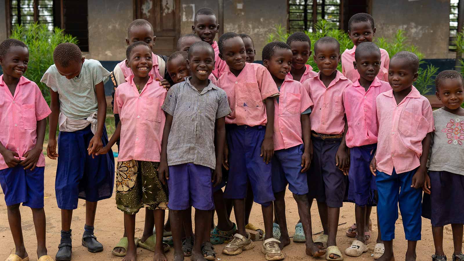 Children in Kenya, many in blue and pink uniforms, posing for a picture in front of their school. 