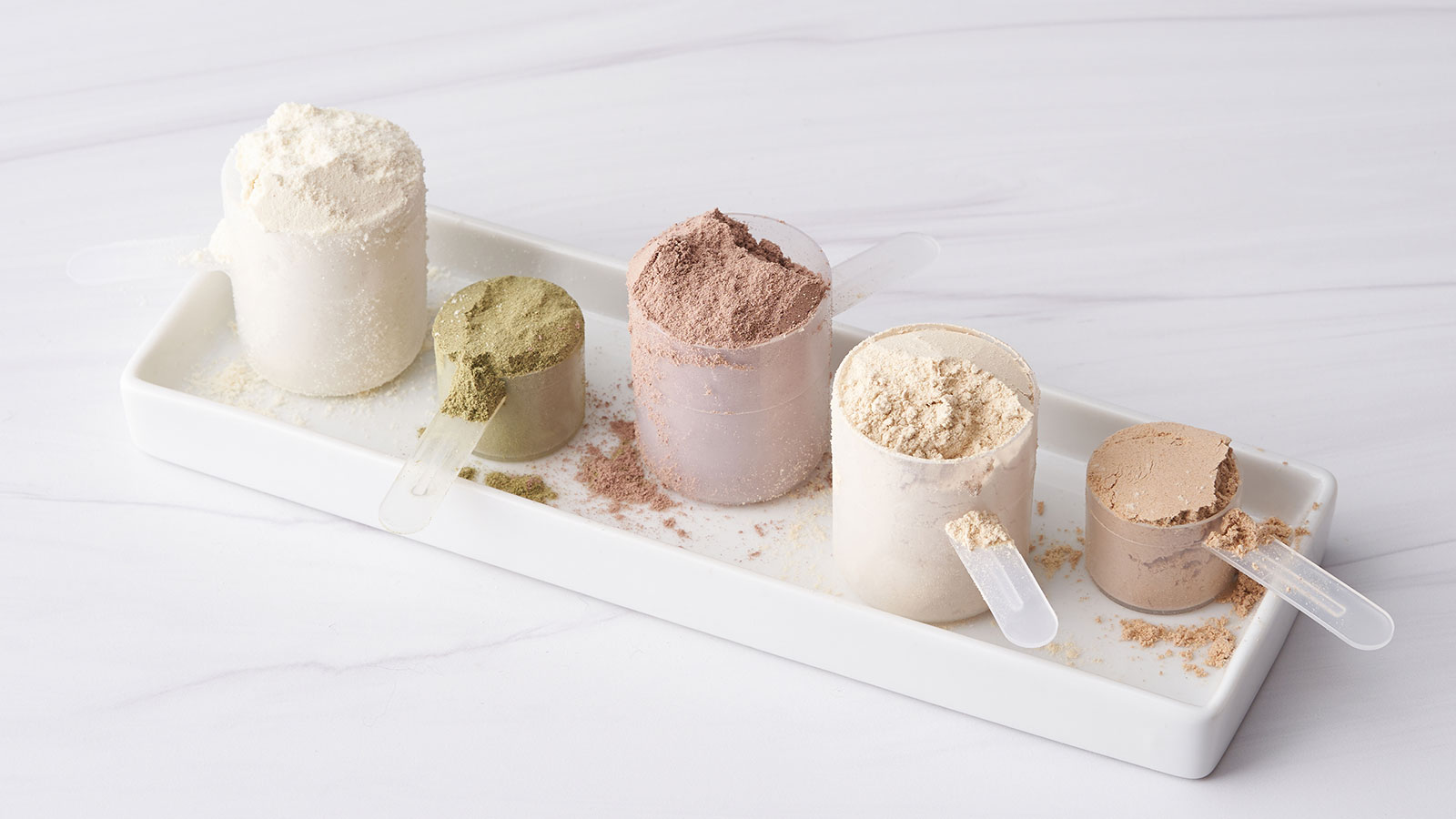 Small, rectangular, white tray, sitting on a white counter. Several measuring cups of protein and greens are sitting on the tray.  