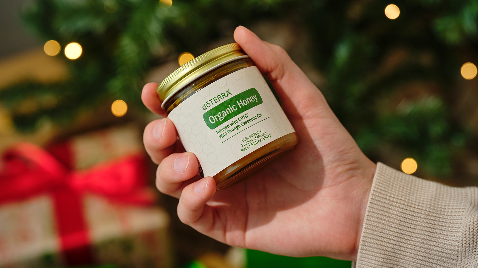 omeone holding the Organic Honey with a lit Christmas tree and wrapped presents beneath them. 