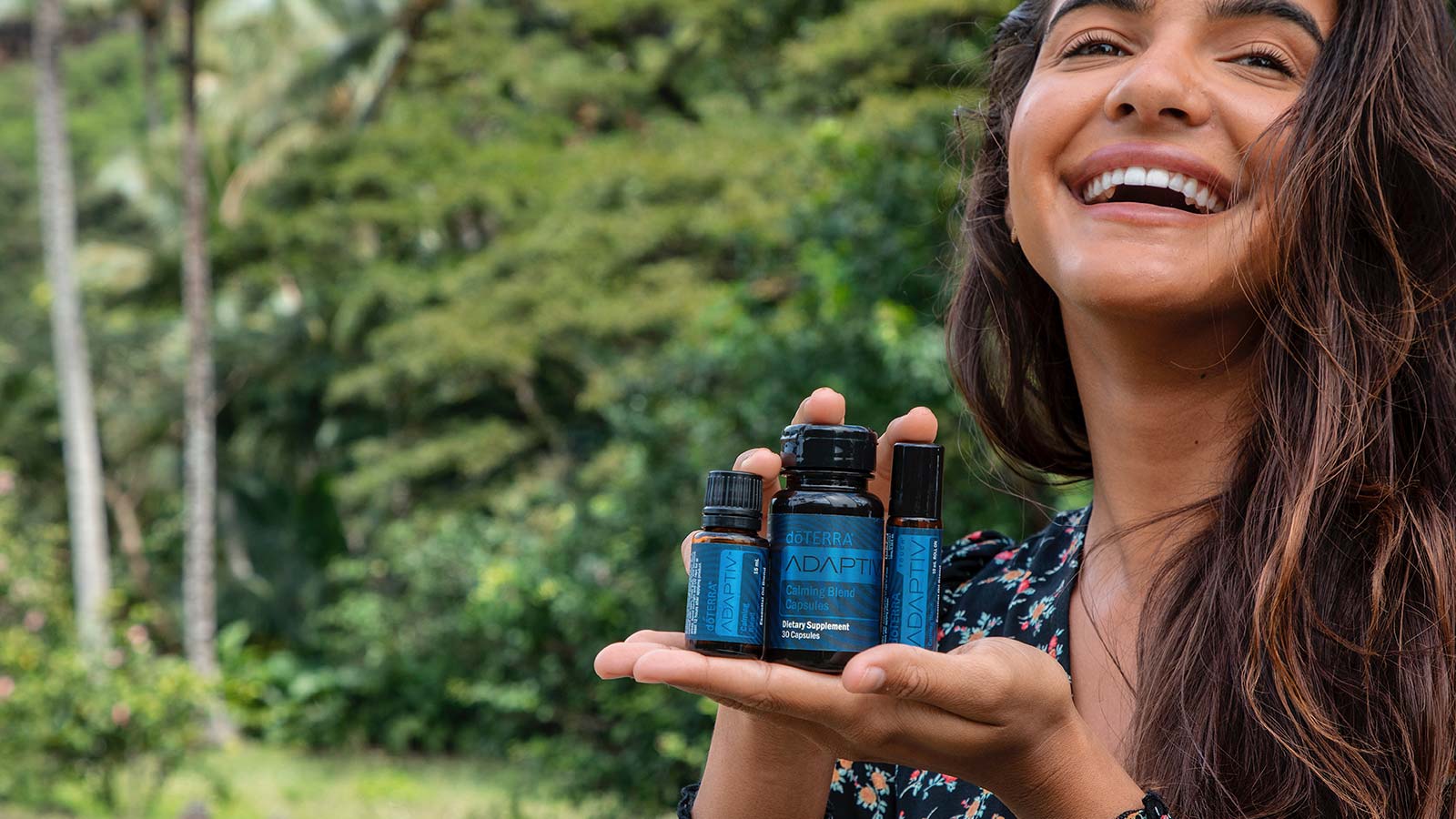 Women smiling, surrounded by trees, and holding Adaptiv Calming Blend Capsules, Adaptiv Calming Blend, and Adaptiv Touch
