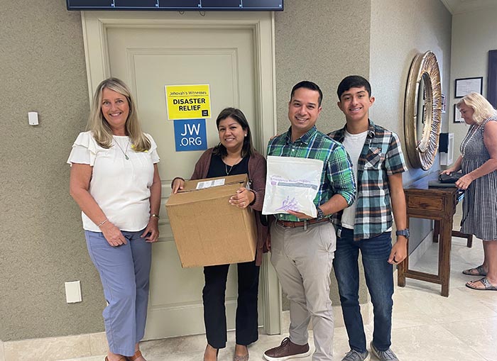 Two men and two women posing for a photo in front of a door. One woman holding a brown box and one man holding a doTERRA 72-Hour Emergency Relief Hygiene Kit. 