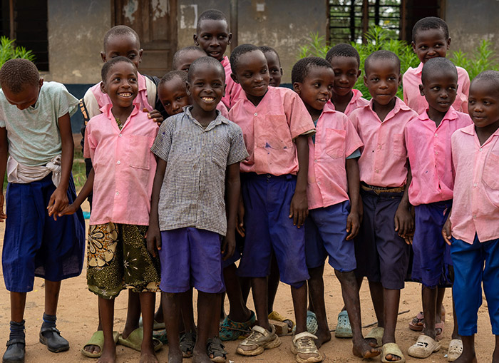 Children in Kenya, many in blue and pink uniforms, posing for a picture in front of their school. 