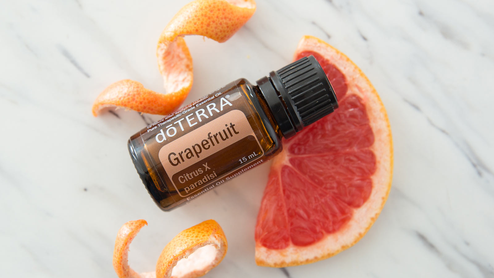 doTERRA Grapefruit essential oil on a marble counter, laying on a slice of grapefruit. Grapefruit rinds sit beside the bottle.  