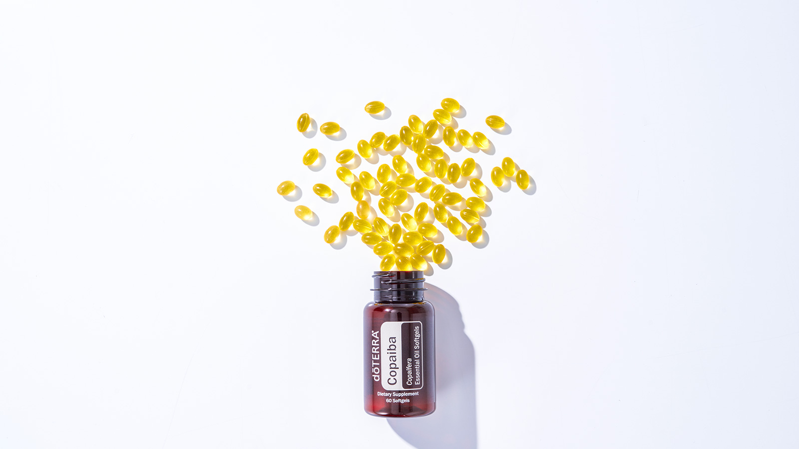 doTERRA’s Copaiba Softgels bottle lying flat on a white background with the softgels spilling out of the bottle.  