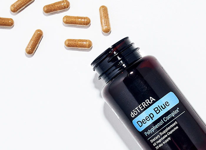 doTERRA Deep Blue Polyphenol Complex bottle lying on a flat surface, with some of the capsules spilling out. 