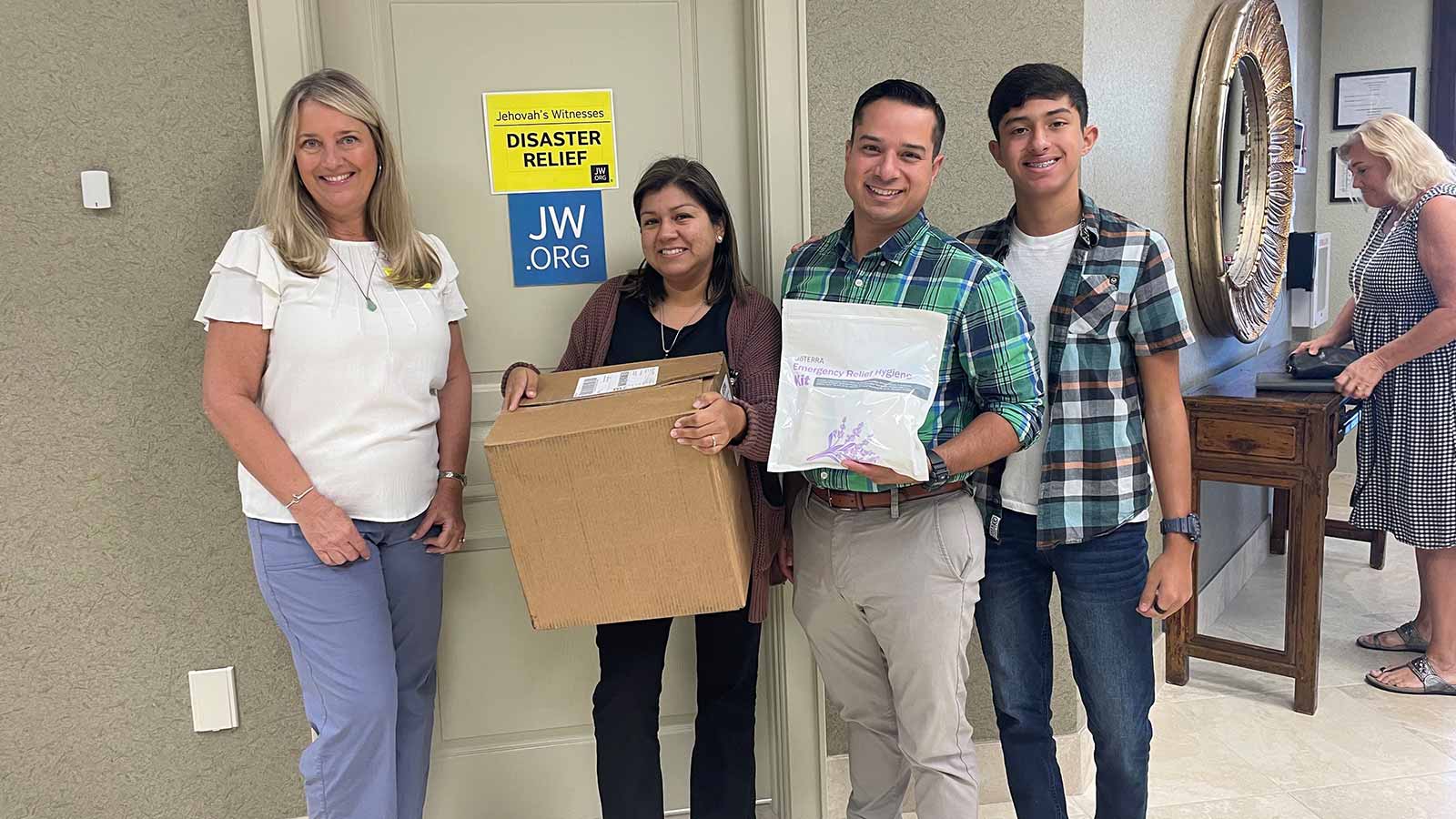 Two men and two women posing for a photo in front of a door. One woman holding a brown box and one man holding a doTERRA 72-Hour Emergency Relief Hygiene Kit. 