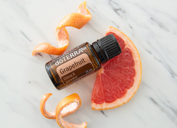 doTERRA Grapefruit essential oil on a marble counter, laying on a slice of grapefruit. Grapefruit rinds sit beside the bottle.  