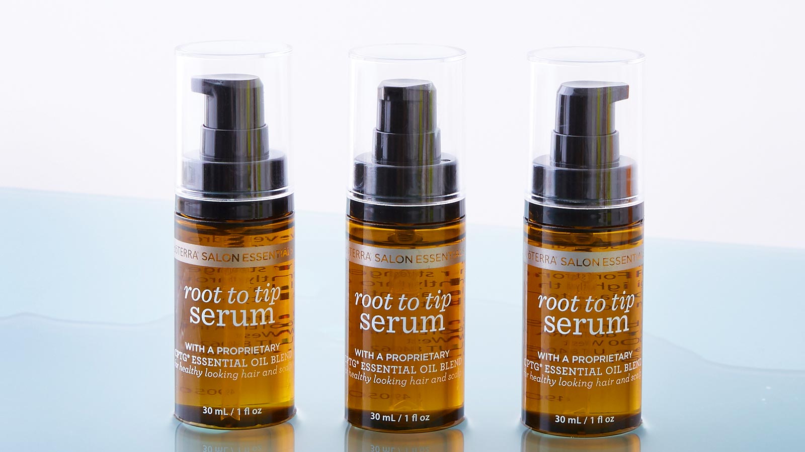 Three bottles of Root to Tip Serum sitting on a wet, light blue surface. 