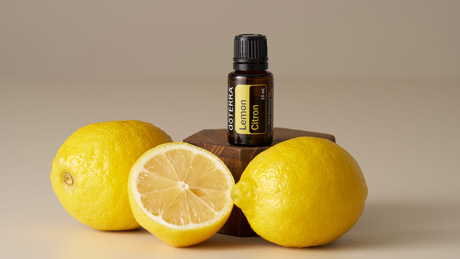 Bottle of doTERRA Lemon essential oil on a small wooden platform, surrounded by two lemons and one cut in half. 