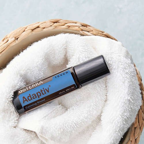 doTERRA Adaptiv Touch roll-on bottle on a white towel in a woven basket with a light blue background.