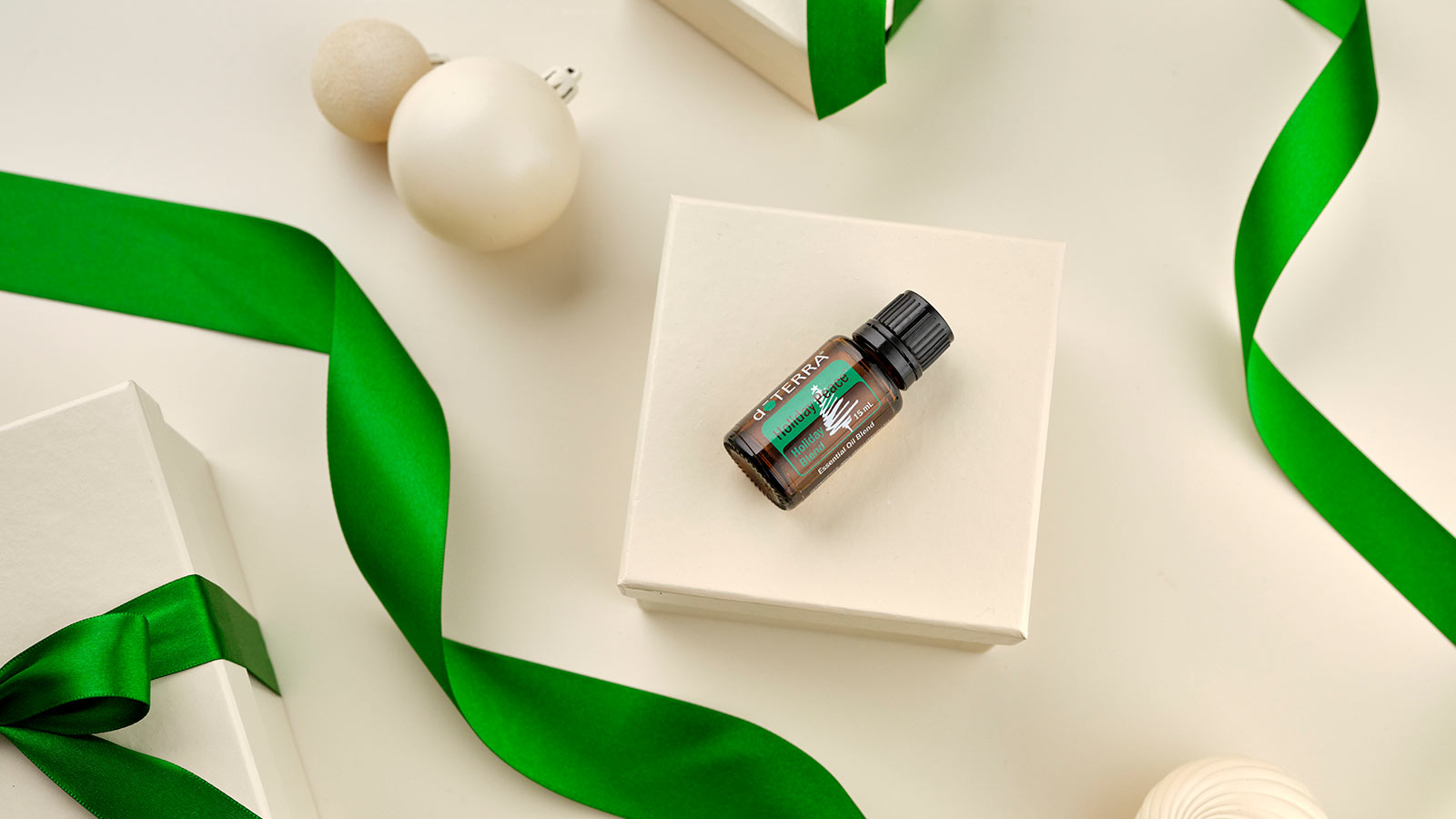 Holiday Joy laying on white box, surrounded by white ornaments and green ribbon. 