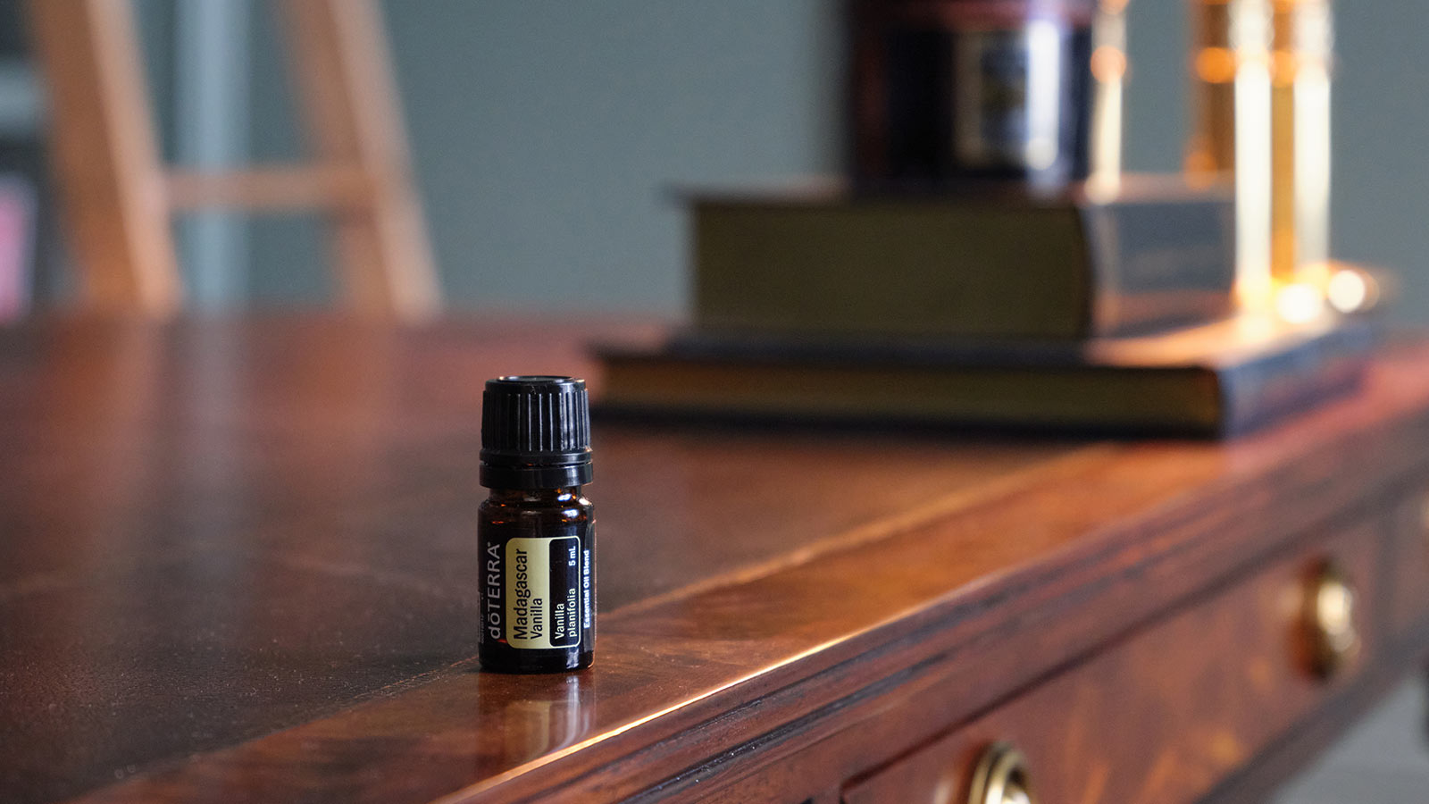 Madagascar Vanilla sitting on wooden desk with a bookshelf ladder in the background and books and a lamp sitting on the desk behind the oil. 