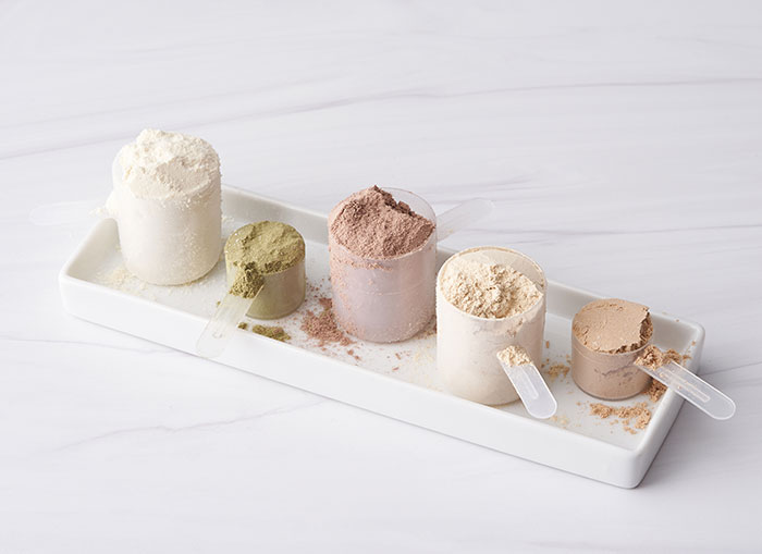 Small, rectangular, white tray, sitting on a white counter. Several measuring cups of protein and greens are sitting on the tray.  