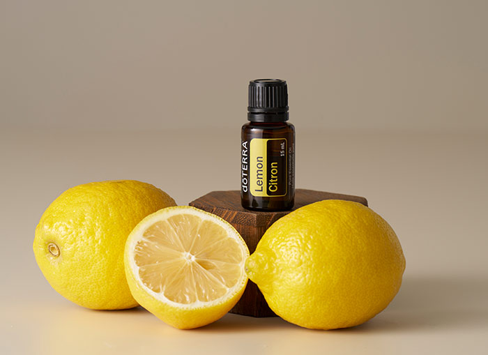 Bottle of doTERRA Lemon essential oil on a small wooden platform, surrounded by two lemons and one cut in half. 