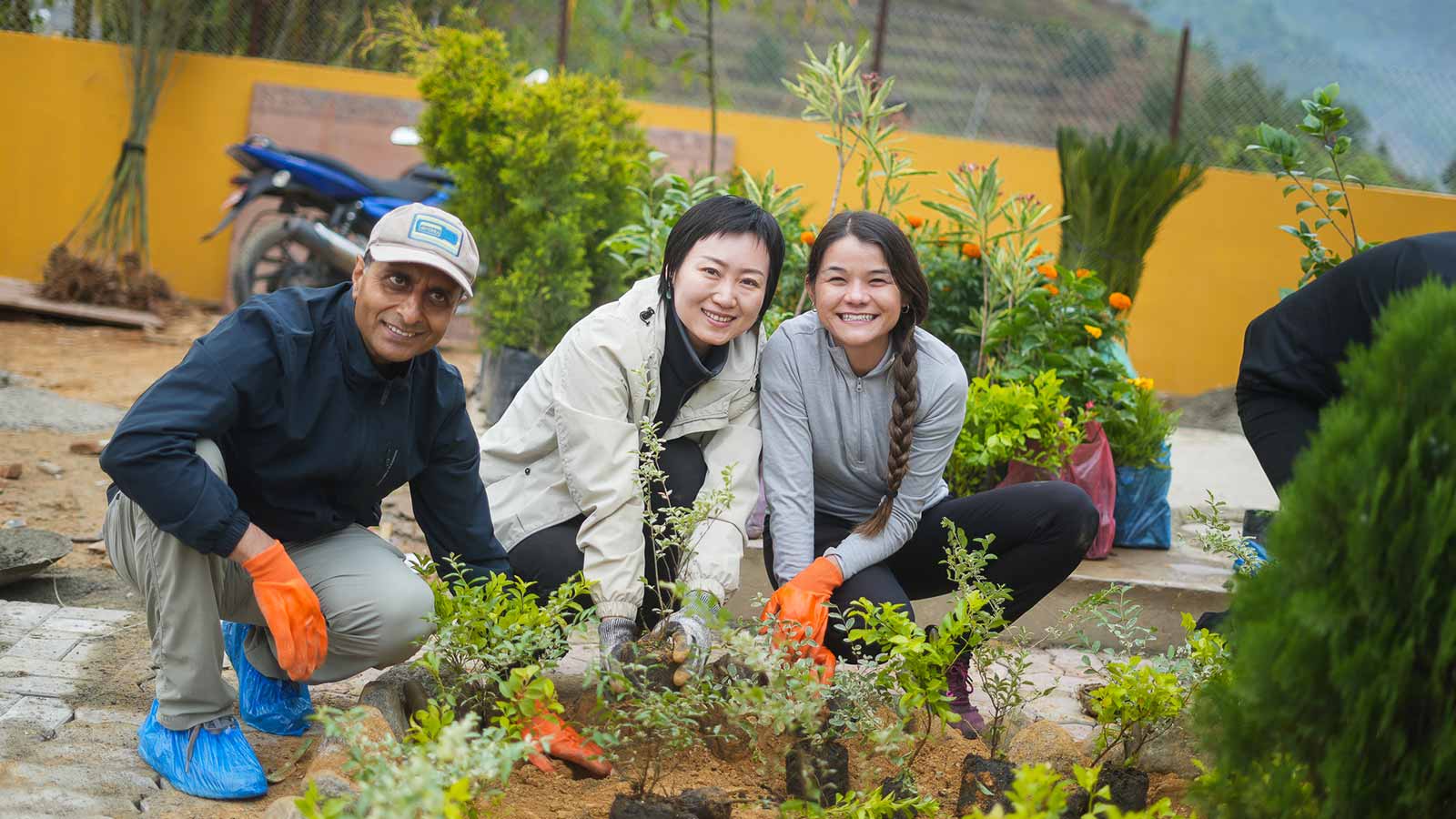 One man and two women squatted down on a cement path in a garden, pause their planting to pose for the photo. 