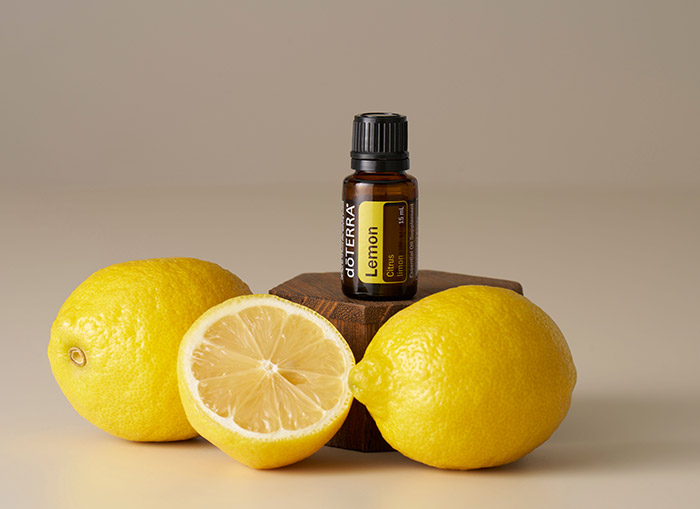 doTERRA Lemon essential oil sitting on raised, wooden surface with lemons surrounding it. 