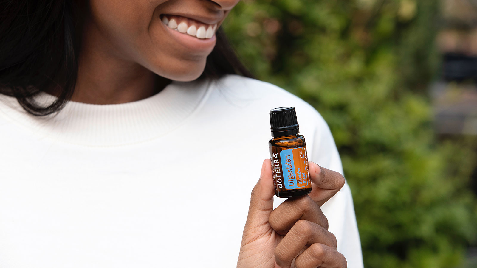 A woman holding doTERRA DigestZen and lifting the side of her shirt with one hand, while rubbing the essential oil on with the other hand. 
