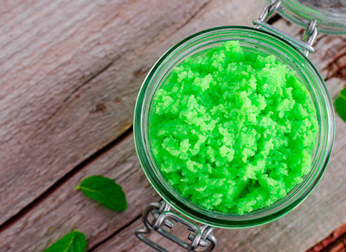 An overhead shot of green sugar scrub in a glass, round jar. The jar is sitting on a wooden surface. 