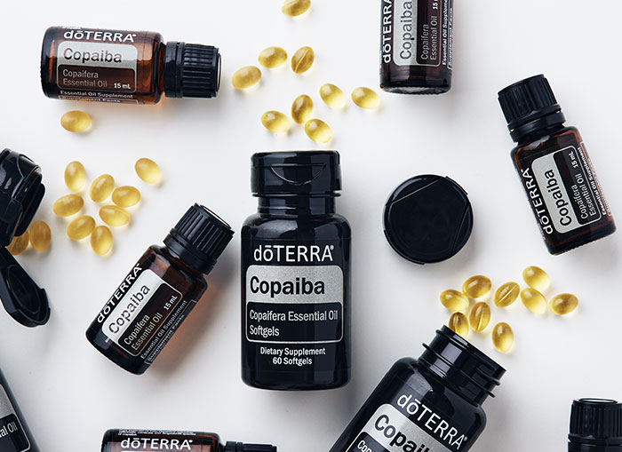 doTERRRA Copaiba essential oil, supplement bottles, and softgels scattered on a white surface. 
