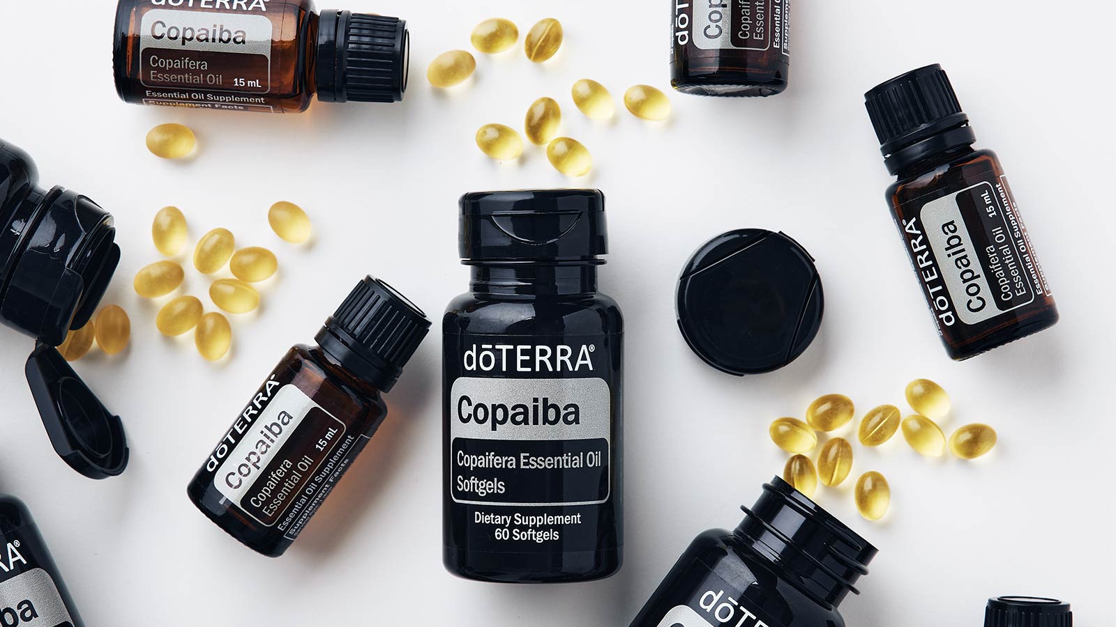 doTERRRA Copaiba essential oil, supplement bottles, and softgels scattered on a white surface. 