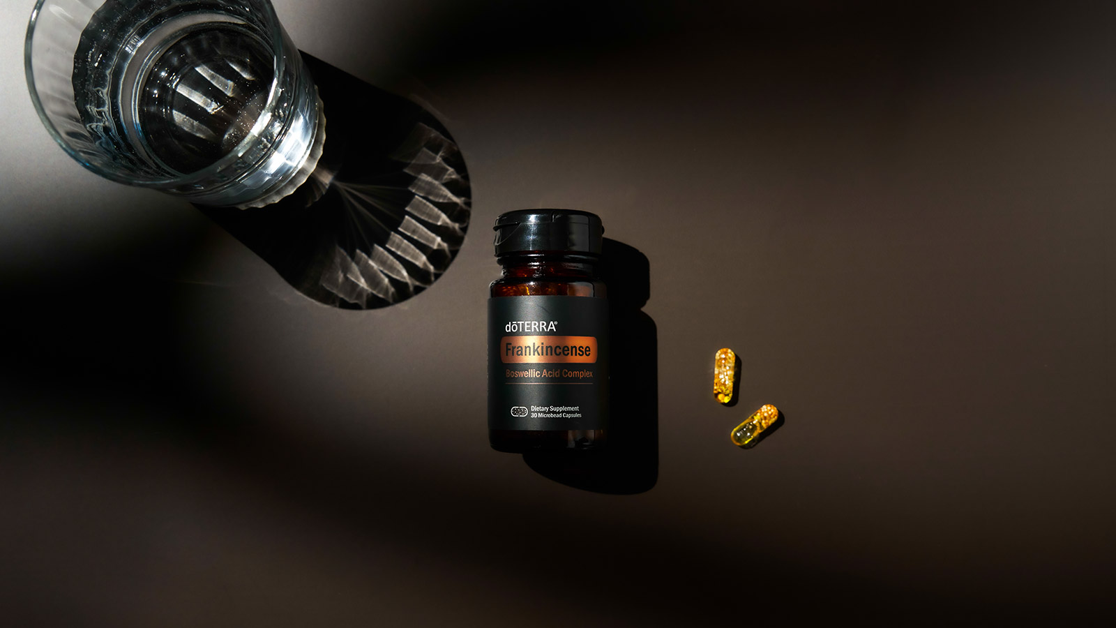 Frankincense Boswellic Acid Complex Capsules laying face up on black background with two capsules on one side and glass of water on the other. 