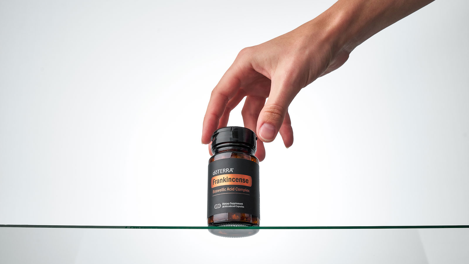 A hand holding a bottle of doTERRA Frankincense Boswellic Acid Complex over a glass table.