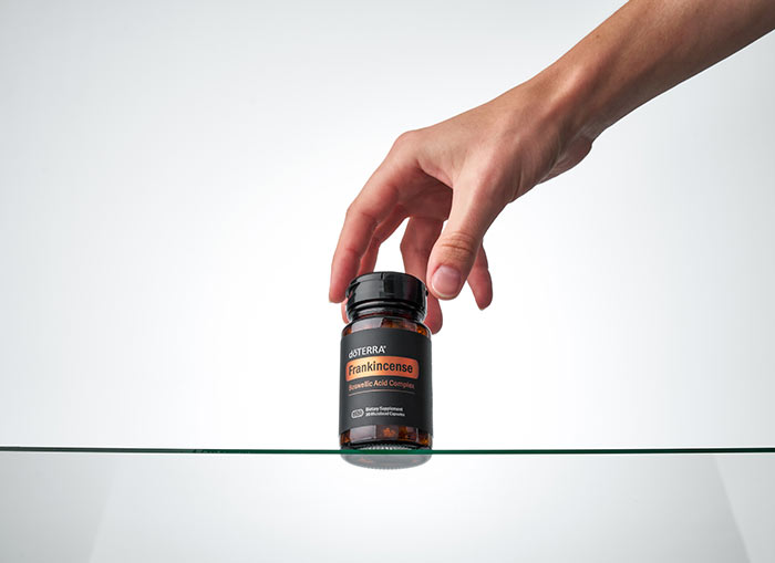 A hand holding a bottle of doTERRA Frankincense Boswellic Acid Complex over a glass table.