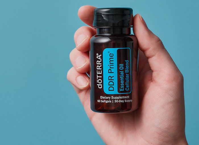 A hand holding doTERRA DDR Prime up to a blue background. 