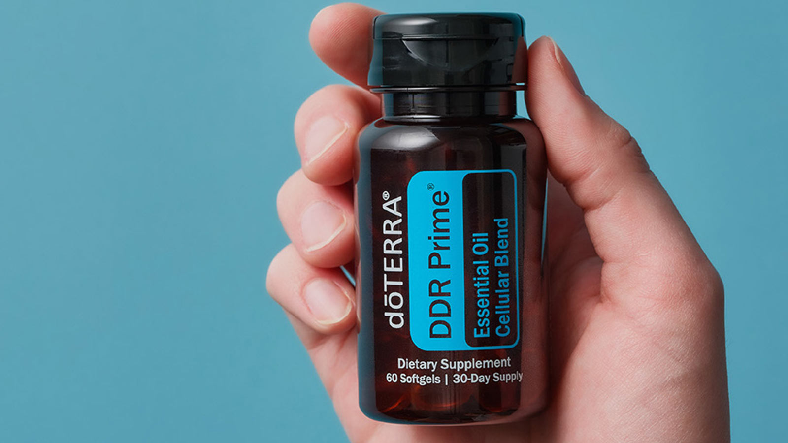 A hand holding doTERRA DDR Prime up to a blue background. 