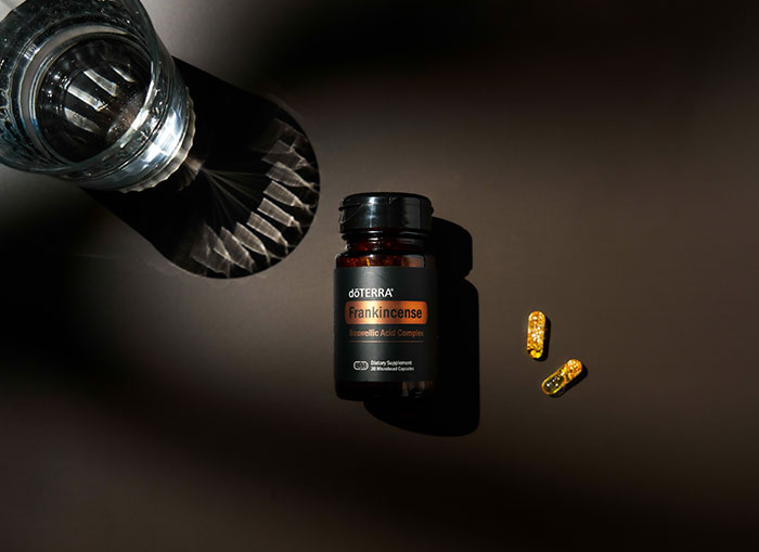 Frankincense Boswellic Acid Complex Capsules laying face up on black background with two capsules on one side and glass of water on the other. 