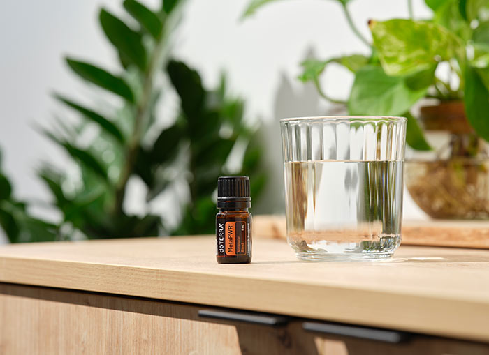 doTERRA MetaPWR essential oil blend sitting on a brown countertop next to a clear glass of water.