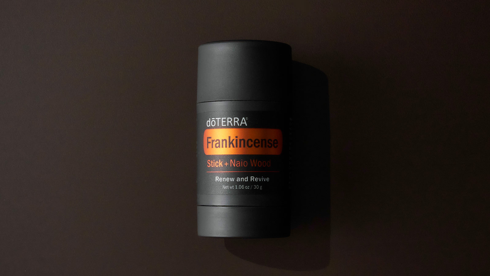 Frankincense Stick + Naio Wood laying on black background. The right side of the bottle slightly shaded.