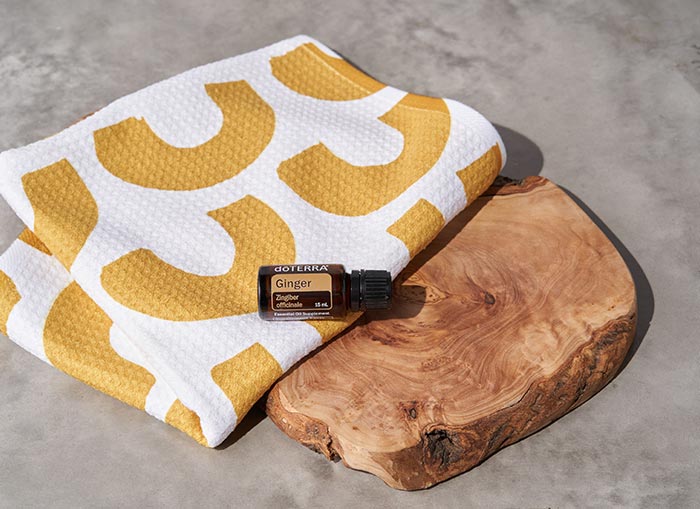 doTERRA Ginger essential oil placed sideways on a yellow and white towel, draped across a flat, wooden, board.  
