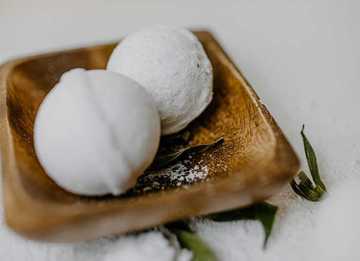 Two, round bath bombs sitting on a brown, rectangular dish. 