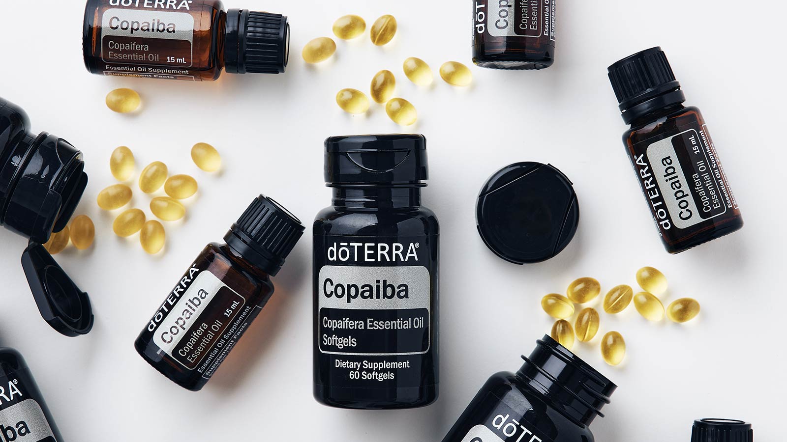 doTERRA Copaiba Softgel bottles and Copaiba essential oil bottles scattered on white surface. 