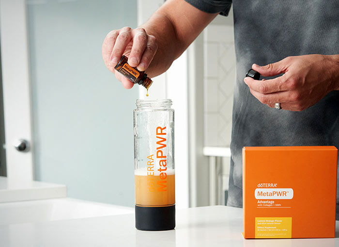 A man pouring doTERRA MetaPWR essential oil blend into a clear water bottle of already mixed doTERRA MetPWR Advantage. A package of MetaPWR Advantage sits to the side of the water bottle. 
