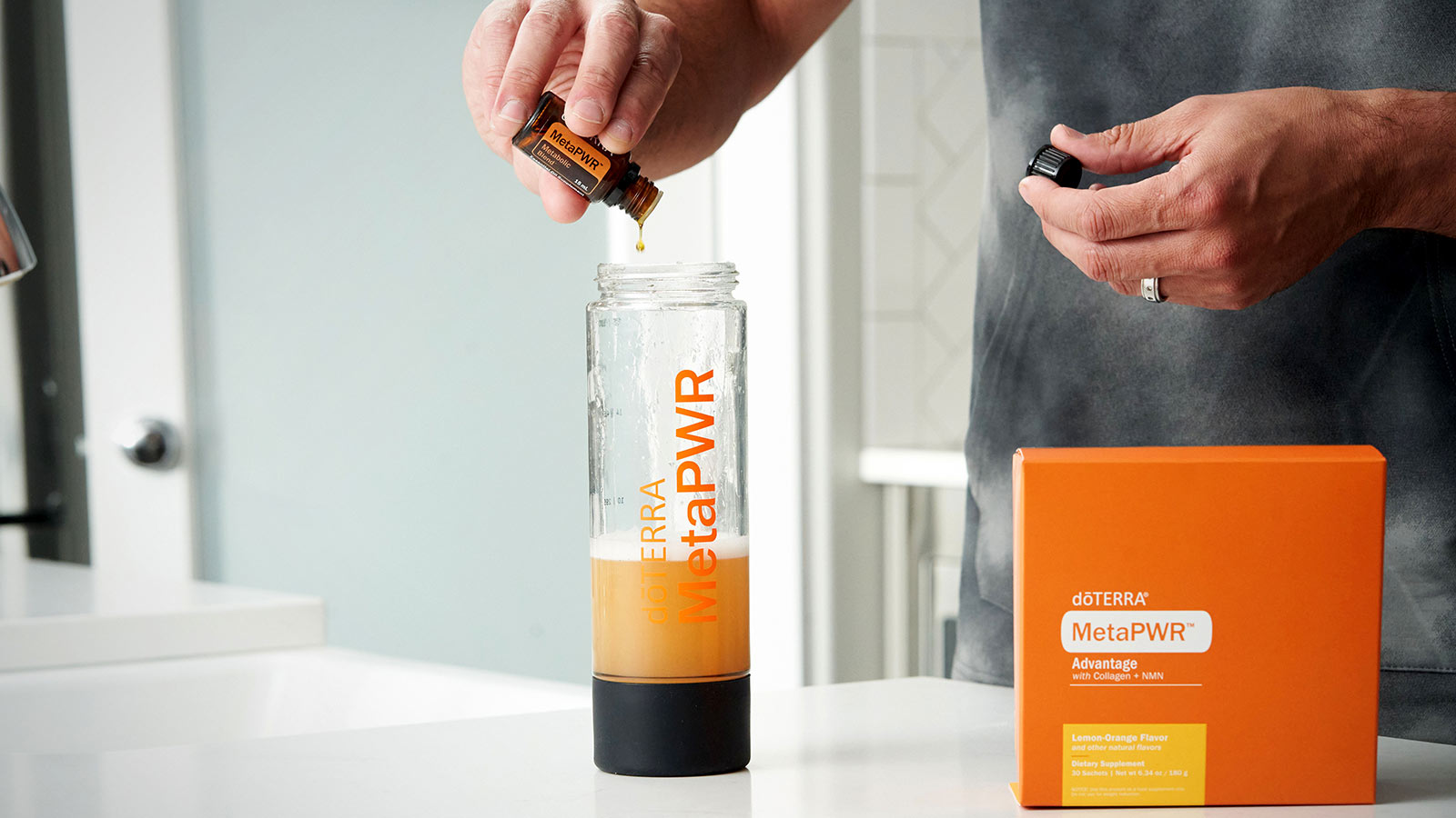 A man pouring doTERRA MetaPWR essential oil blend into a clear water bottle of already mixed doTERRA MetPWR Advantage. A package of MetaPWR Advantage sits to the side of the water bottle. 