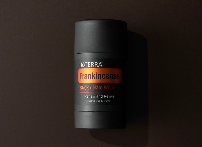 Frankincense Stick + Naio Wood laying on black background. The right side of the bottle slightly shaded.