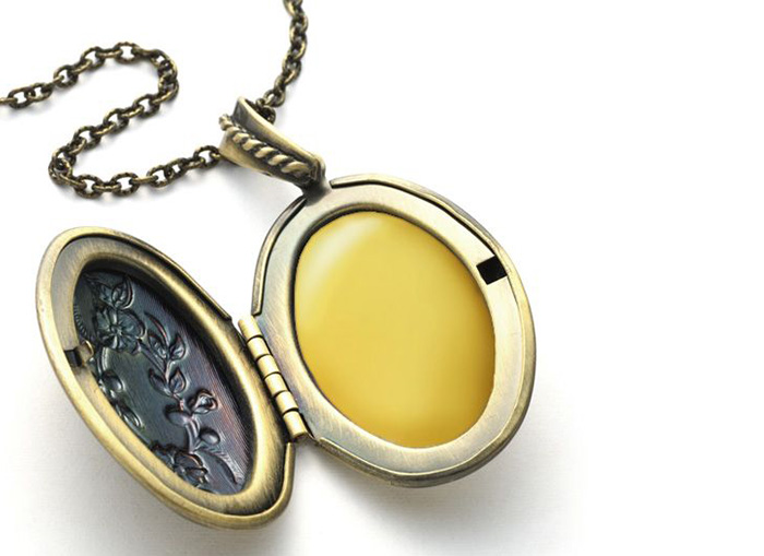 An oval-shaped, golden locket sits open, flowers carved on one side of the chain resting above the locket. 