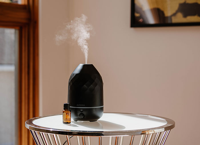 Volo Onyx Diffuser sitting on a white, round table. Mist coming out. A doTERRA Clementine essential oil bottle sitting beside it. 