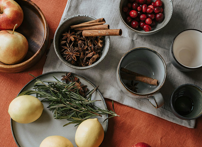Apples, lemons, cranberries, and other seasonings in cups and plates sitting on a table. 