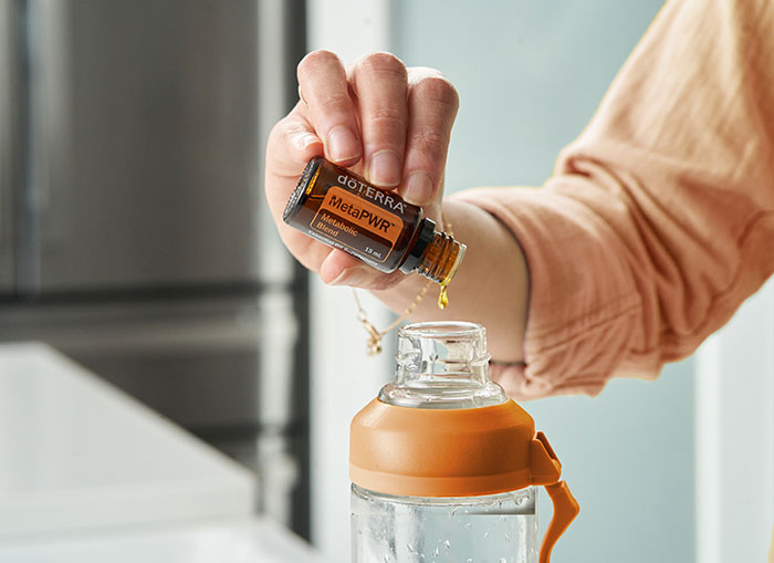 Someone holding a bottle of doTERRA MetaPWR essential oil blend, pouring into a clear water bottle.
