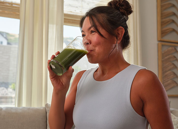 Women sitting on a couch near a window, drinking VMG+ from a glass cup.