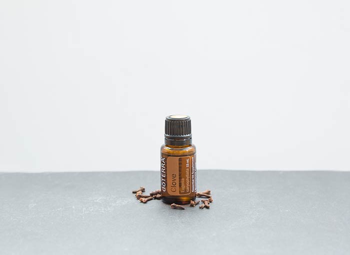 doTERRA Clove essential oil seated on a gray surface with clove buds scattered around it.  